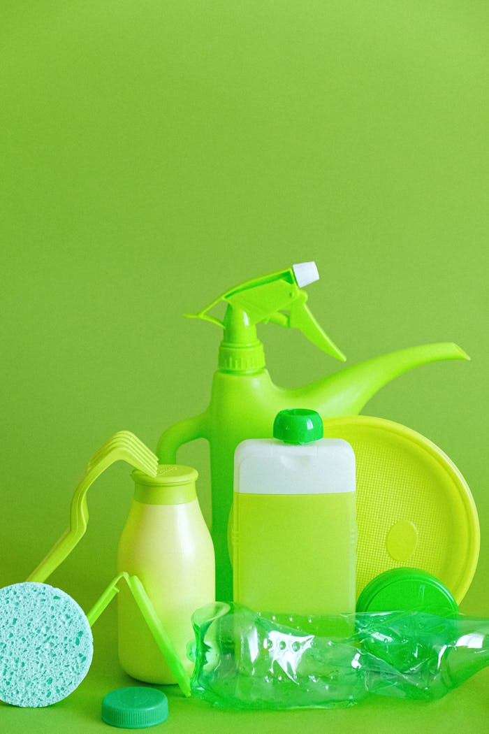 Assorted green cleaning supplies against vibrant green backdrop, promoting eco-friendly sanitation.